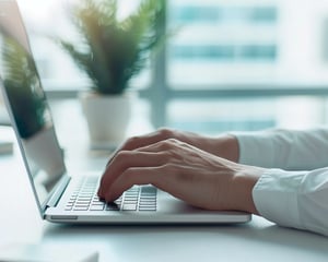 A close-up of hands typing on a laptop keyboard at a desk, with a softly blurred office background, representing everyday office work, digital productivity, and modern business operations.
