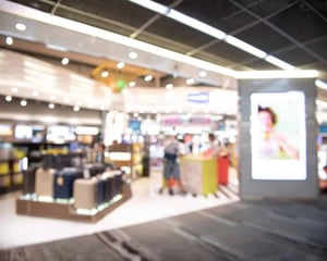 A blurred view of a modern retail store with luggage displays and digital signage, illustrating travel retail operations supported by cloud-based infrastructure.