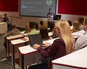 Students seated in a university lecture hall using laptops during a class, illustrating digital learning, classroom technology, and higher education IT environments.