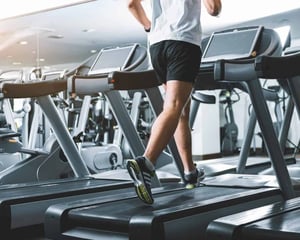 A person runs on a treadmill in a modern gym, with multiple cardio machines visible, representing fitness operations supported by reliable technology and IT services.