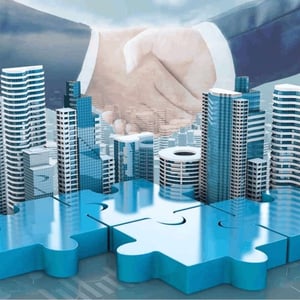 Two business people shaking hands with a city and puzzle pieces below as symbols of coming together in business