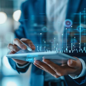 A business professional holds a tablet and stylus while interacting with a floating digital chart of bars and data points, representing real-time analytics, performance monitoring, and data-driven decision-making.