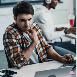 A man sitting at a desk looking at a laptop..
