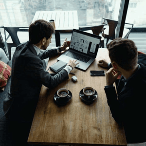 A technology expert sitting at a desk showing information to another man.
